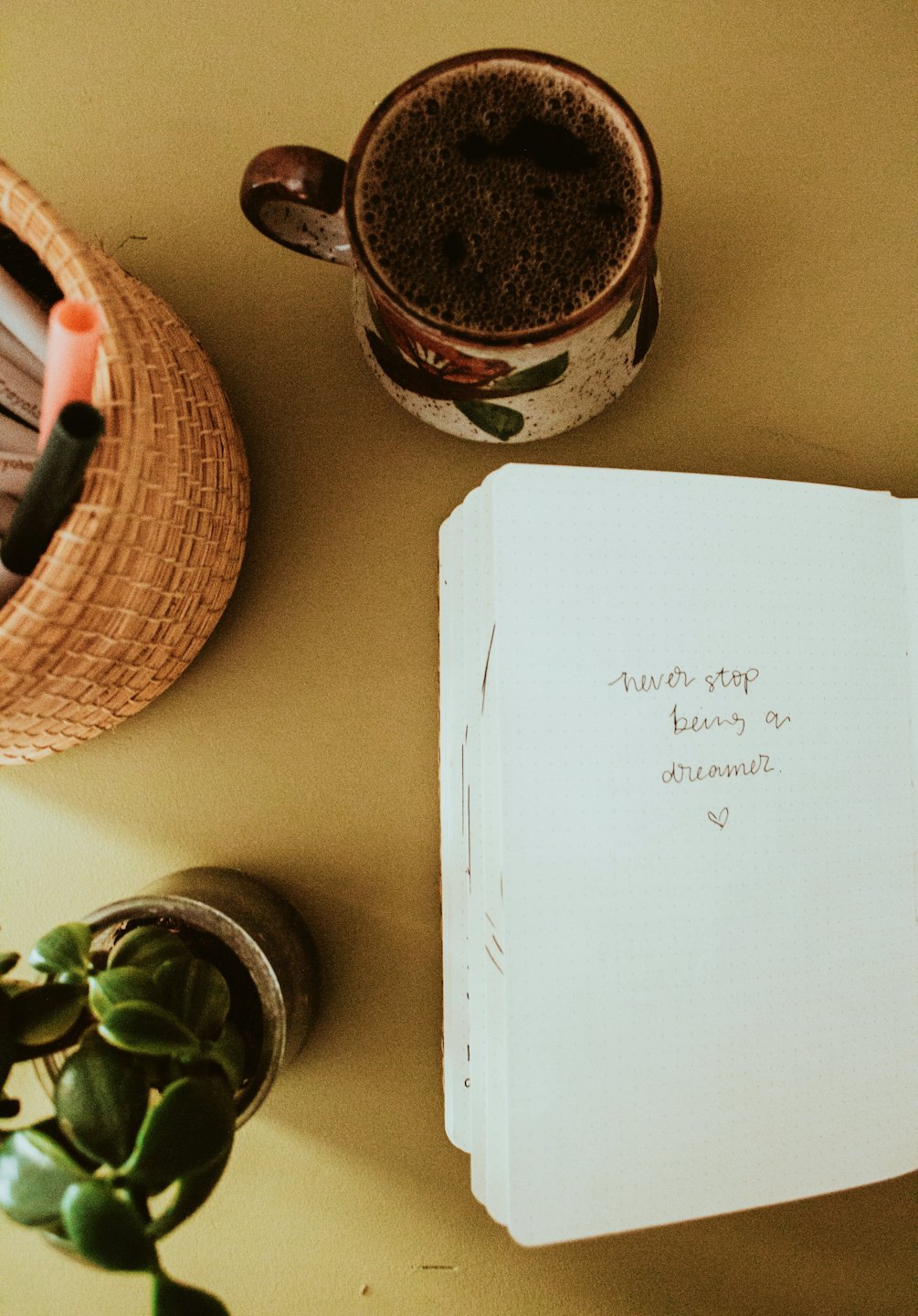Coffee mug, journal, pens, and plant on a desk.